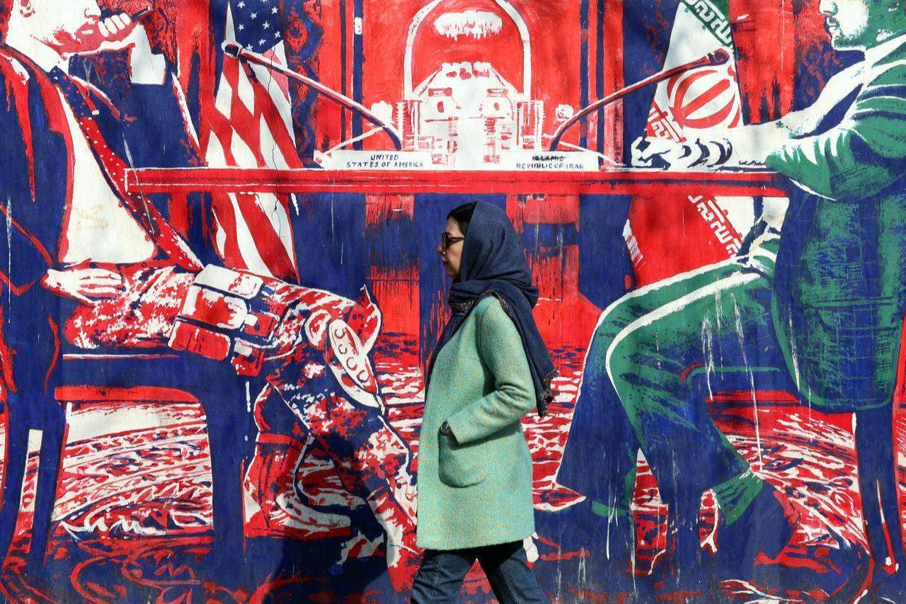 An Iranian woman walk past anti-US mural depicting Iran and US negotiation table, painted on the outer walls of the former US embassy, in Tehran, February 6, 2026. (AFP Photo)