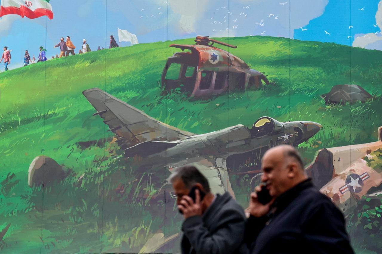 Iranian men speaking on their mobiles walk past a huge anti-US billboard displayed on a building in Tehran's Valiasr Square, February 8, 2026. (AFP Photo)