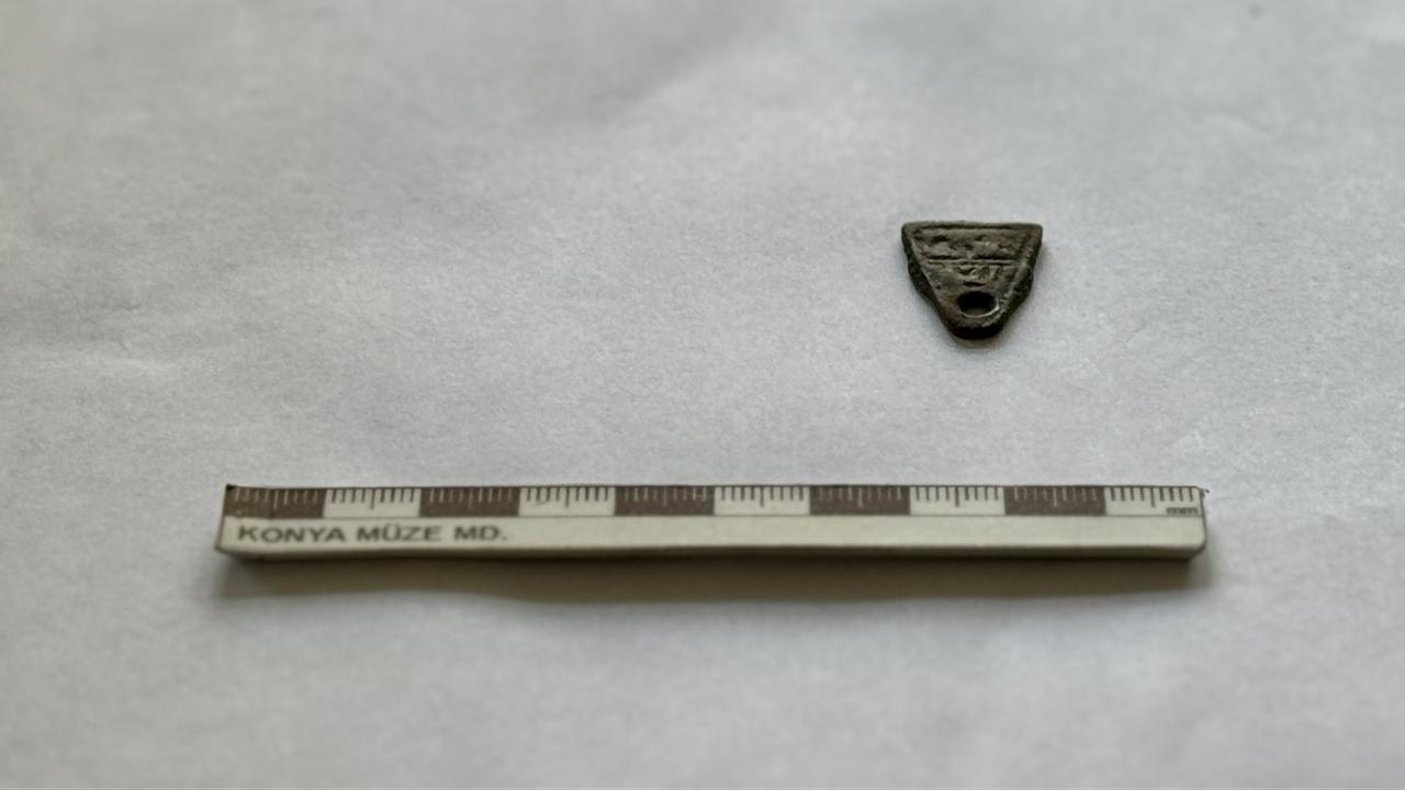 A bronze triangular amulet believed to date to the Seljuk period is shown with a measurement scale after being uncovered at Lystra, Konya, Türkiye, Feb. 9, 2026. (AA Photo)