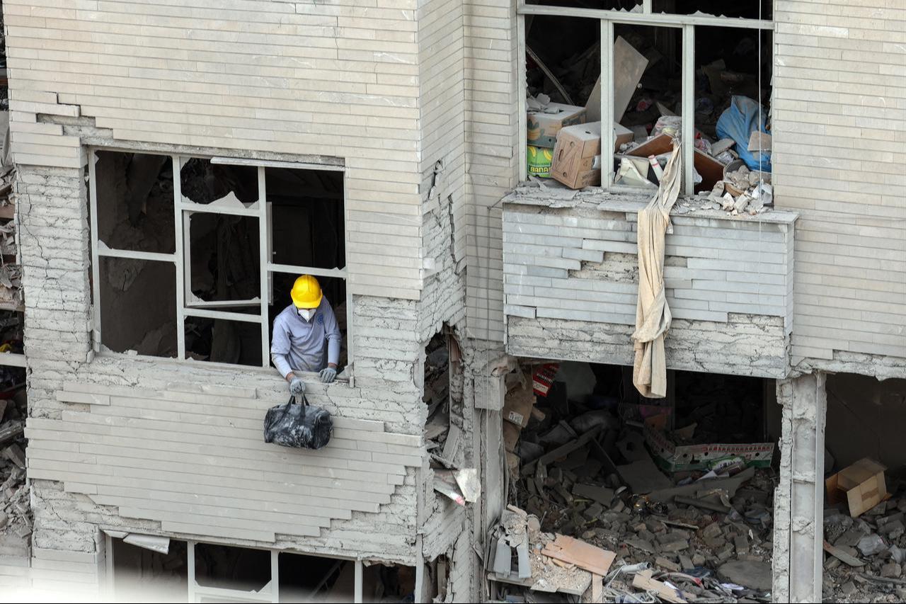 A man stands at the shattered window of a destroyed residential building as residents collect belongings from the rubble in Tehran, March 12, 2026. (AFP Photo)