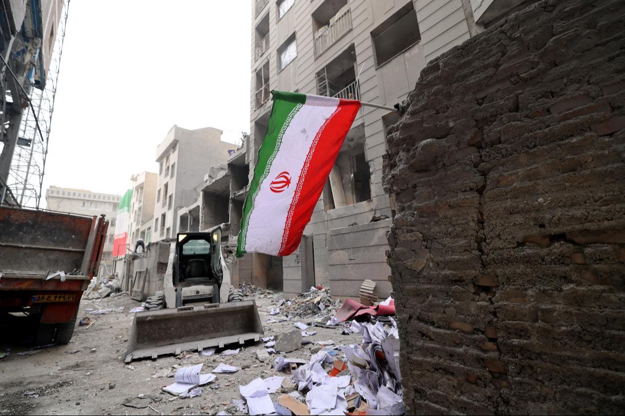 An Iranian flag flutters as a digger arrives to help remove the debris from destroyed buildings following a military strike on the Iranian capital Tehran, March 15, 2026. (AFP Photo)