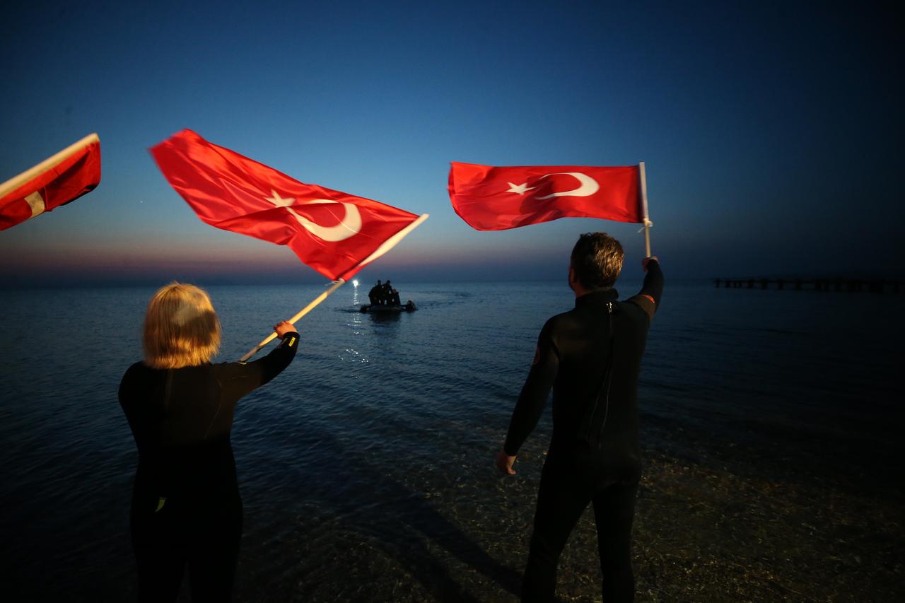 Supporters wave Turkish flags on the shore as a boat carrying divers approaches the coast following Mazlum Kibar’s Guinness World Record attempt for the longest scuba dive in cold water at Anzac Cove in Canakkale, Türkiye, March 15, 2026. (AA Photo)