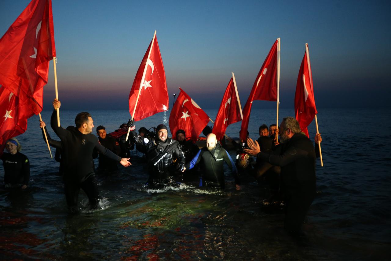 Professional diver Mazlum Kibar (C) is welcomed by supporters carrying Turkish flags after completing his Guinness World Record attempt for the longest scuba dive in cold water at Anzac Cove in Canakkale, Türkiye, March 15, 2026. (AA Photo)