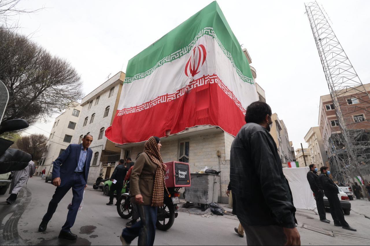 A huge Iranian flag adorns a building as Iranians walk past damaged structures following an earlier military strike in the Iranian capital, Tehran, on March 15, 2026. (AFP Photo)
