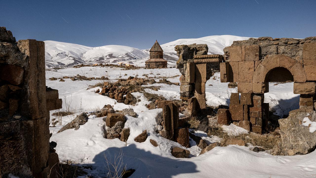 Snow-covered ruins at the UNESCO-listed Ani archaeological site in Kars, with a historic church visible in the background, Türkiye, February 11, 2026. (AA Photo)