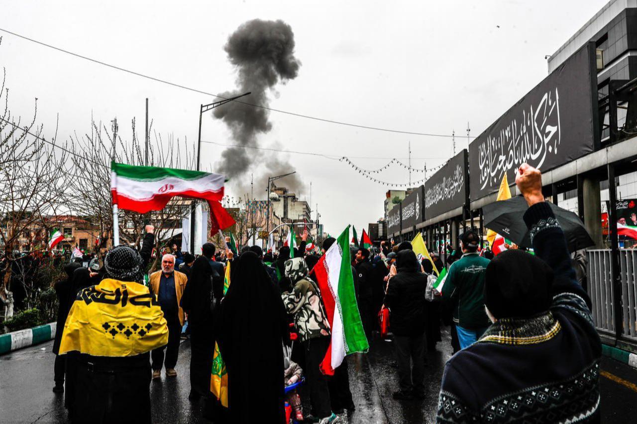 Smoke rises after an explosion during the World Quds Day march as participants carry Iranian flags and banners in Tehran, Iran, on March 13, 2026. (Iranian President's Press Office / AA Photo)