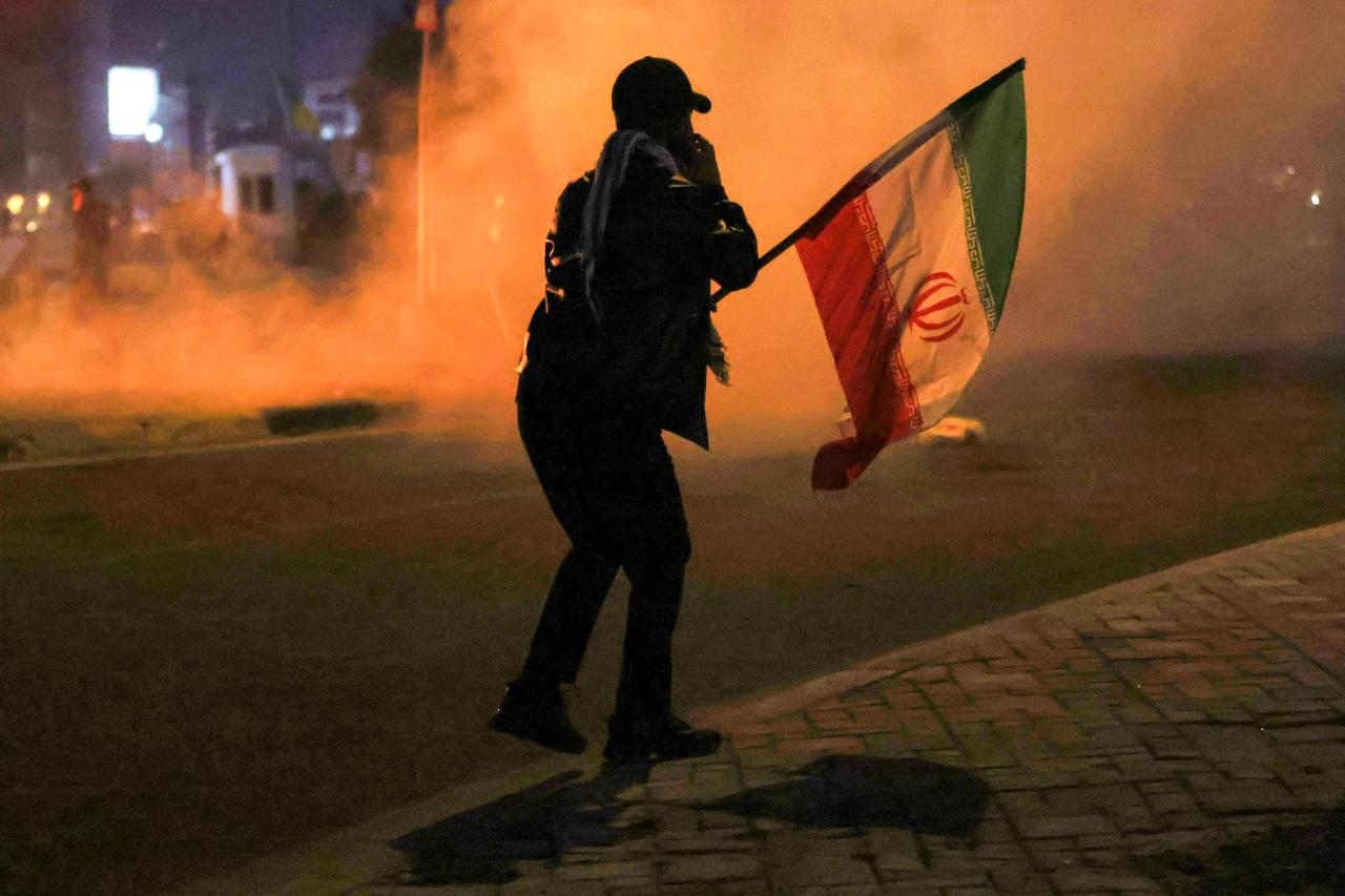 A person waving an Iranian flag walks near tear gas fumes as protesters clash with Iraqi security forces as they try to approach Green Zone in Baghdad, March 1, 2026. (AFP Photo)