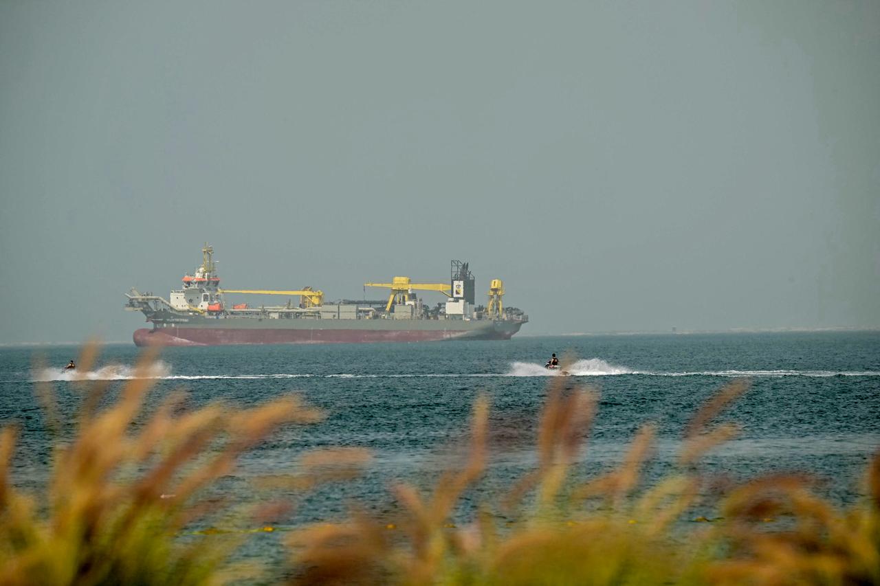 Bathers ride jet skis past anchored cargo ships off the coast of Dubai on March 2, 2026. (AFP Photo)