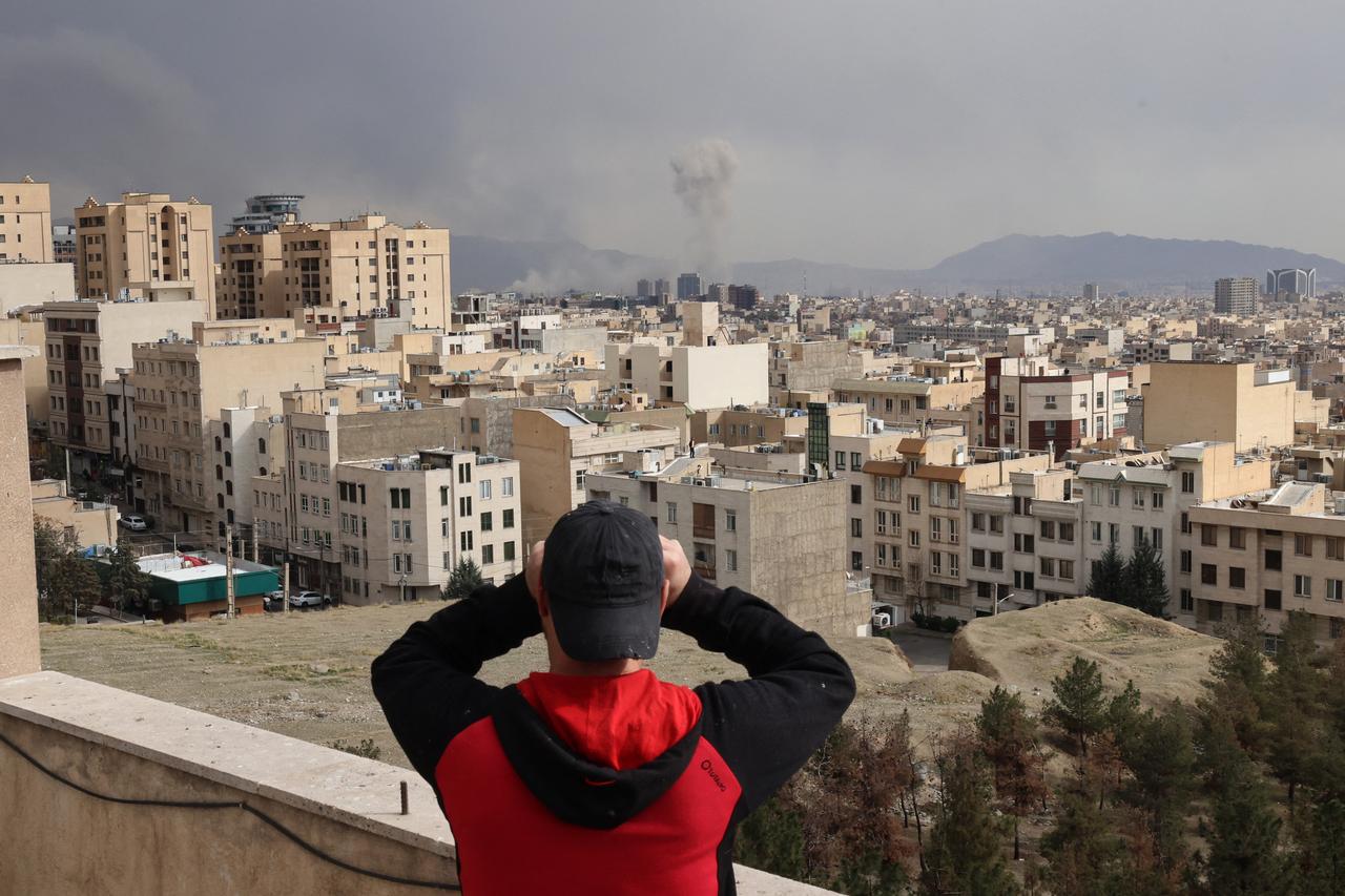A man looks through biculars as a plume of smoke rises after a military strike on the capital Tehran on March 2, 2026. (AFP Photo)