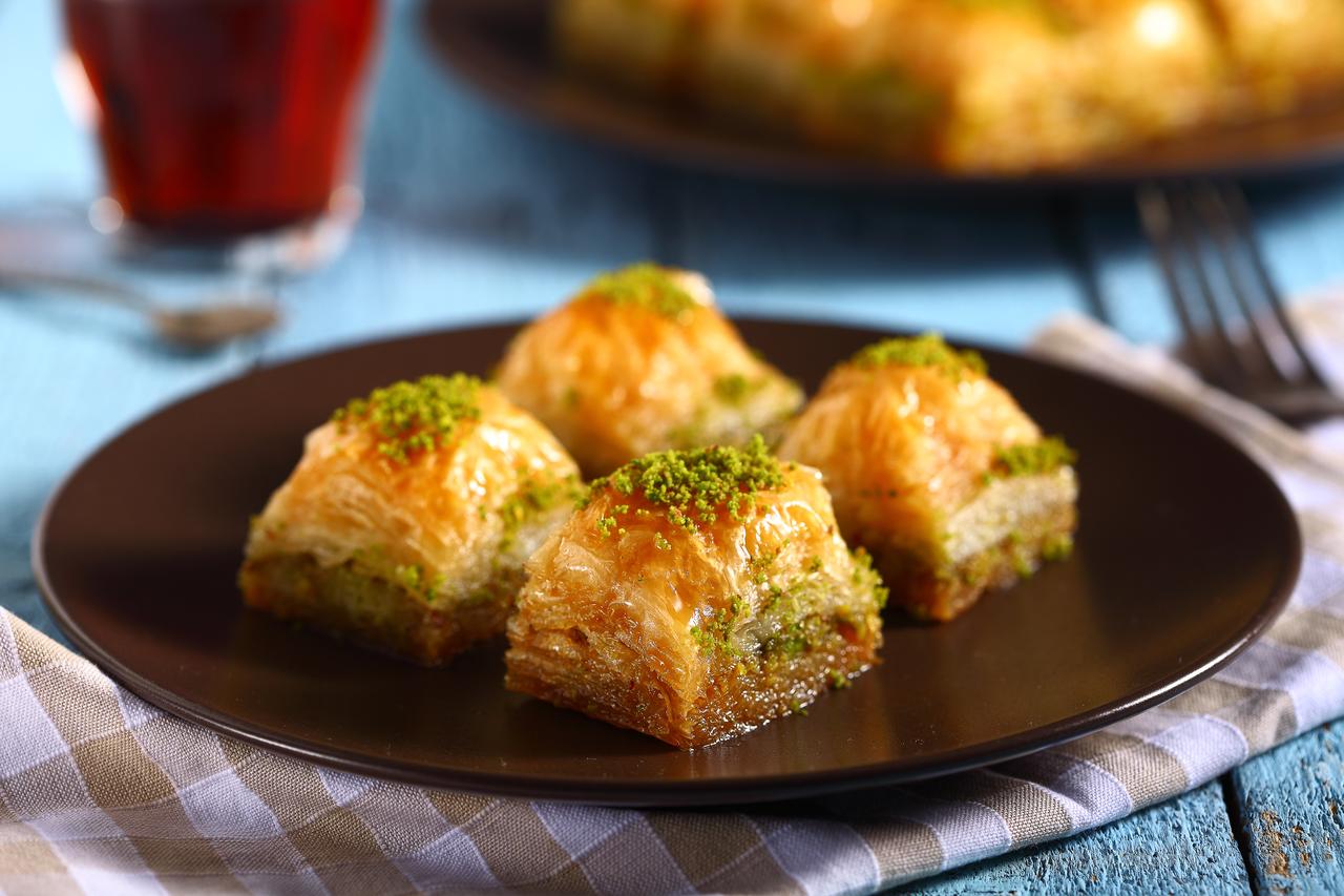 Pistachio baklava served on a plate alongside a glass of tea. (Adobe Stock Photo)