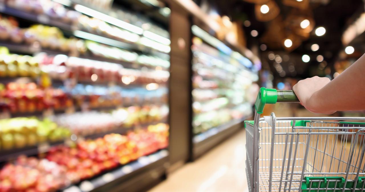 A woman pushing a shopping cart in a grocery store. (Adobe Stock Photo)