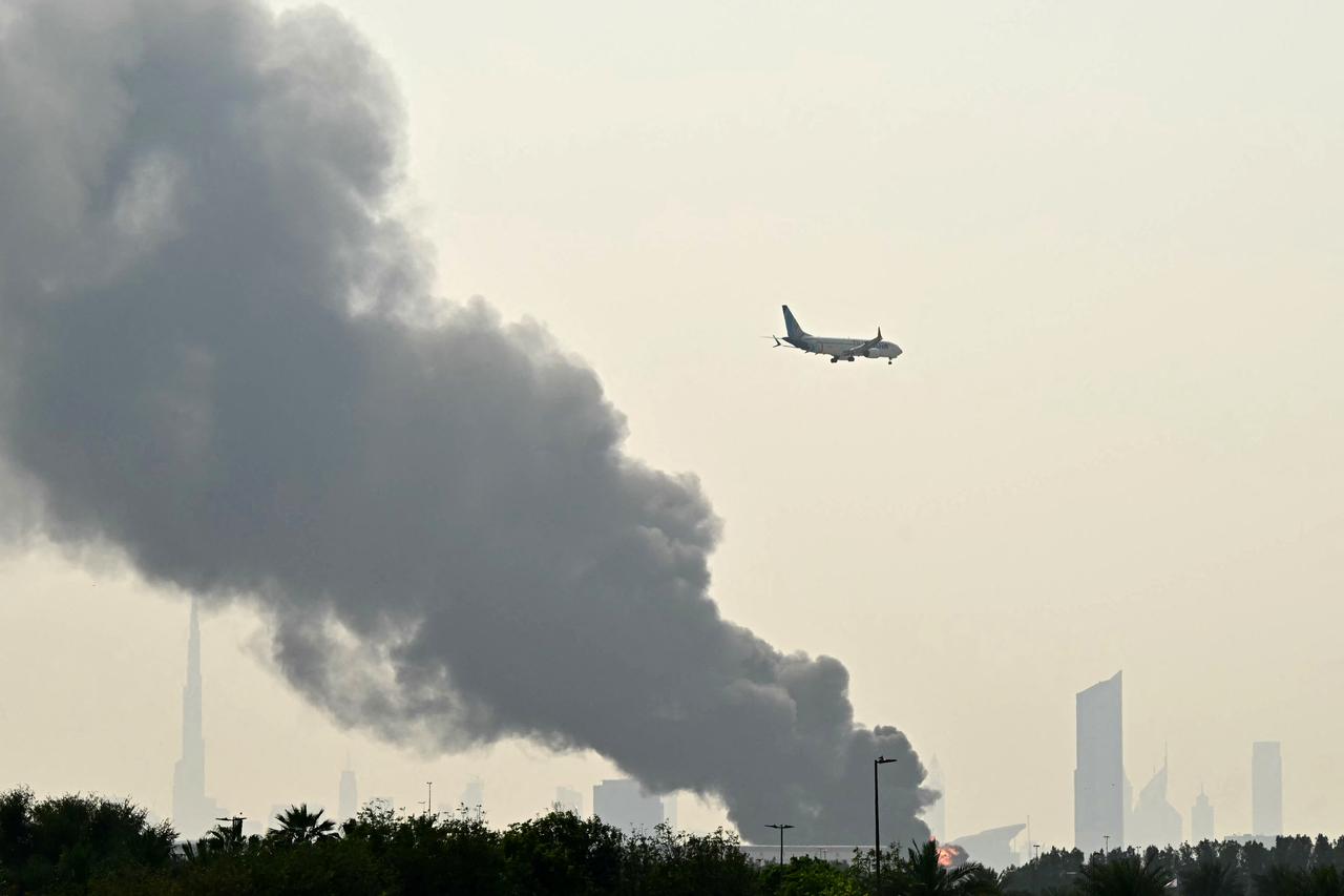 An Emirates aircraft flies past plumes of smoke from an ongoing fire near Dubai International Airport in Dubai on March 16, 2026. (AFP Photo)