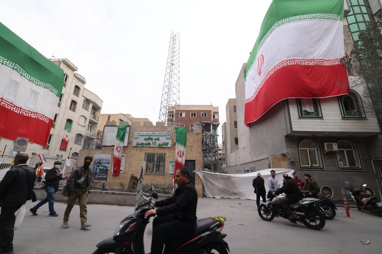 A huge Iranian flag adorns a building as Iranians walk past damaged structures following an earlier military strike in the Iranian capital, Tehran, March 15, 2026. (AFP Photo)