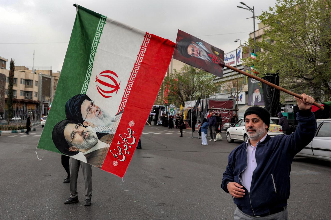 A man holds an Iranian flag showing the faces of Iran's late and new Supreme Leaders Ali and Mojtaba Khamenei along Enghelab (Revolution) Square in central Tehran on March 25, 2026. (AA Photo)