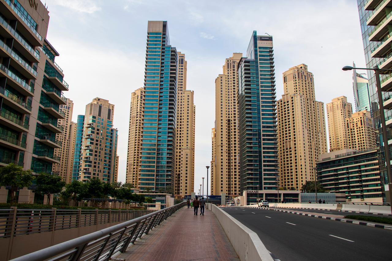 Pedestrians walk along a street lined with high-rise residential towers in Dubai, United Arab Emirates. (Adobe Stock Photo)