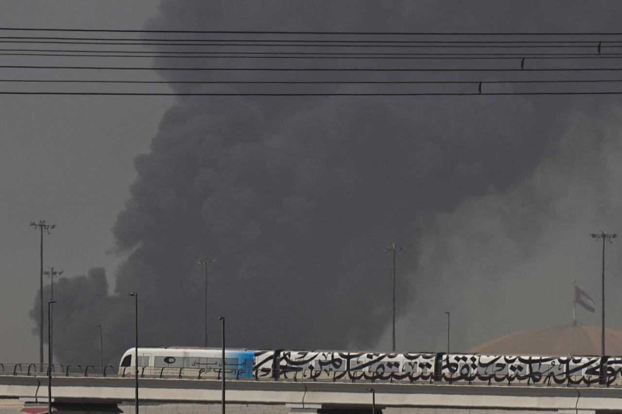 A metro train passes by a plume of smoke rising from the port of Jebel Ali following a reported Iranian strike in Dubai on March 1, 2026. (AFP Photo)