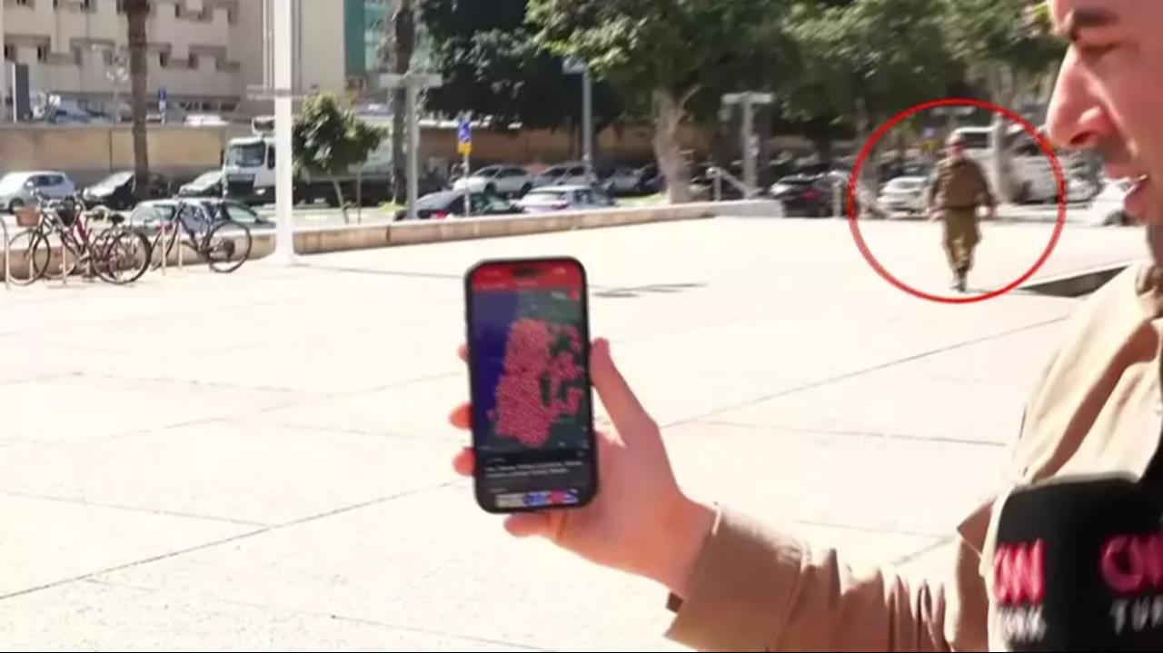 The CNN TURK reporter shows a mobile screen displaying missile alerts moments before security forces intervene in Tel Aviv. (Photo via CNN TURK)