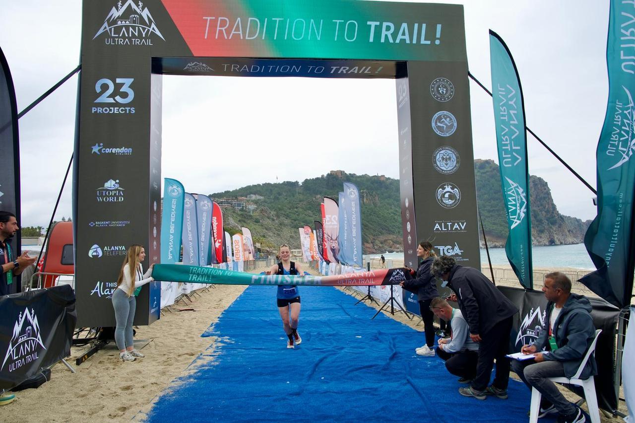 A runner crosses the finish line on Cleopatra Beach after completing her race at Alanya Ultra Trail, marking the end of a demanding coastal-to-mountain course, Alanya, Türkiye. (Photo via Alanya Ultra Trail)