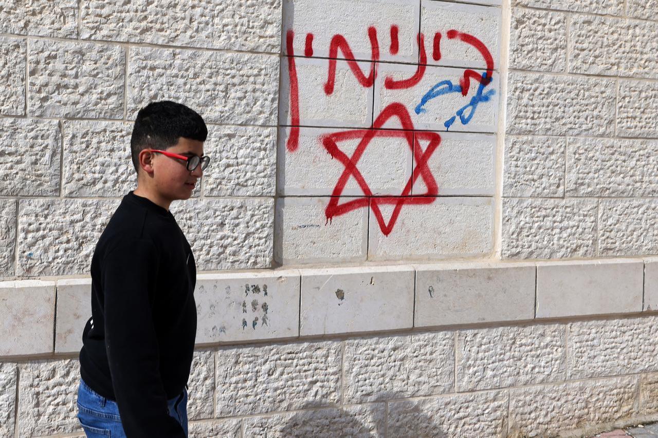 A Palestinian boy walks past an offensive Hebrew graffiti on the walls of a damaged house following a reported attack by Israeli settlers in Jalud village, south of Nablus in the occupied West Bank, on March 22, 2026. (AFP Photo)