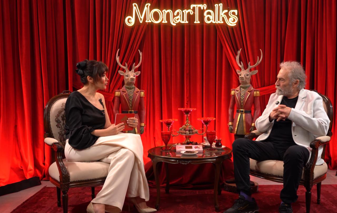 Haluk Bilginer and the host during a MonarTalks interview session, set in a stylized studio with red curtains and decorative elements, March 2026. (Photo via YouTube/@boldagencyprojects)