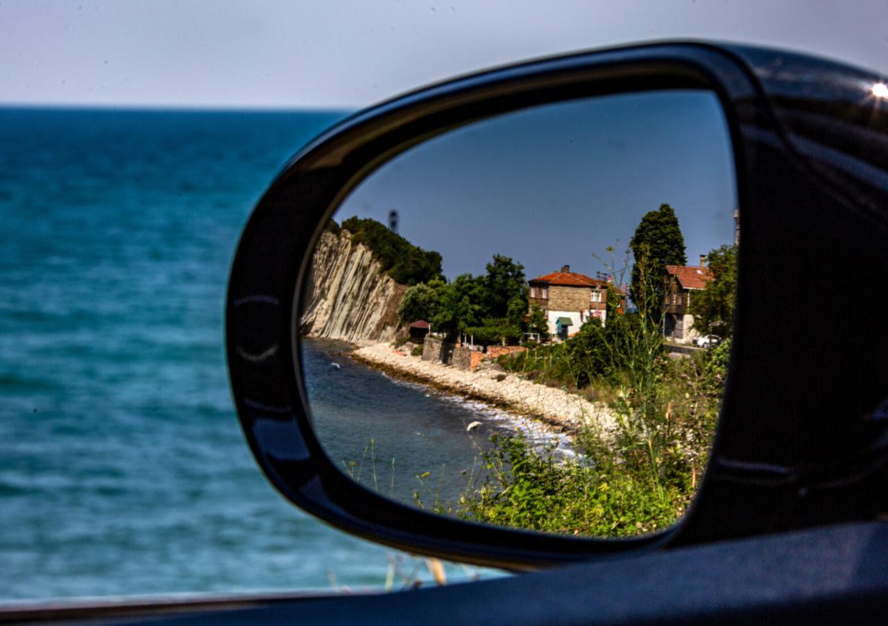 A coastal village near Kiyikoy reflected in a car’s side mirror, with the Black Sea and rocky cliffs in the background. (Adobe Stock Photo)