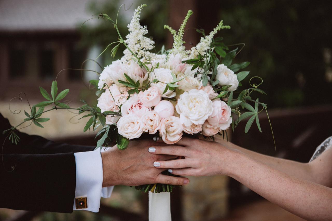 The bride and groom hold a bouquet of pink and white flowers with green leaves during their wedding ceremony, accessed on Sept. 16, 2025. (Adobe Stock Photo)