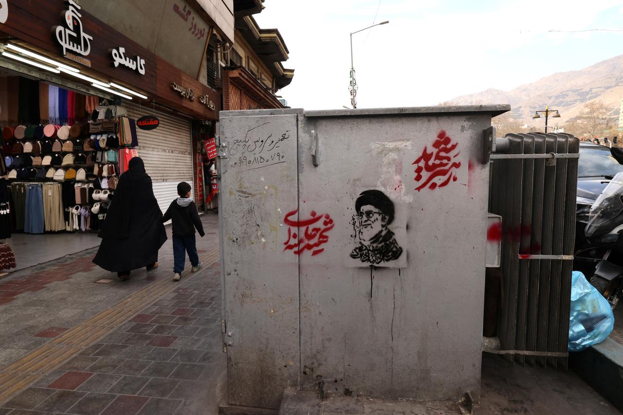 An Iranian woman holds a hand of a boy as they walks past a shop and an image of Iran's slain supreme leader Ali Khamenei, along a street at the Tajrish Square in Tehran, Iran on March 7, 2026. (AFP Photo)