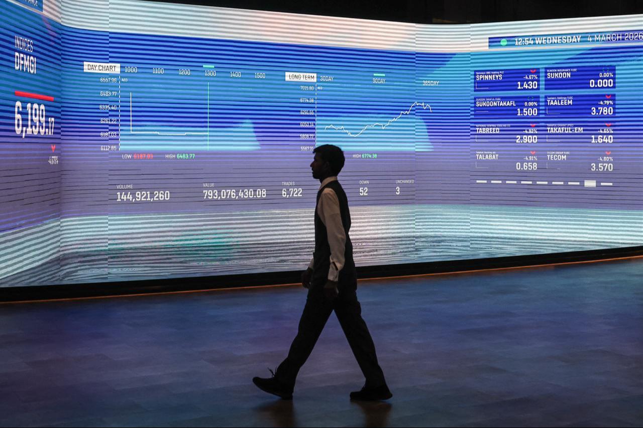 A man walks past a screen displaying stock indices at the Dubai Financial Market (DFM) stock exchange in Dubai, March 4, 2026. (AFP Photo)