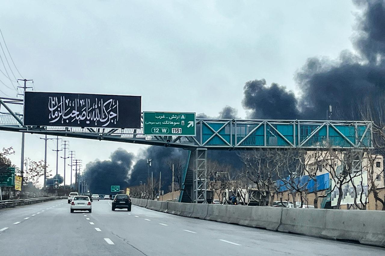 Vehicles move along a highway near plumes of black smoke billowing in Tehran on March 8, 2026. (AFP Photo)