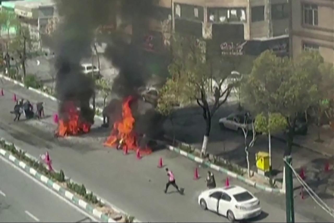 This video grab taken from UGC images posted on social media on March 17, 2026, appears to show a motorcycle ablaze following a strike on a Basij checkpoint in Tehran, as people pull a person away from the fire. (Photo by various sources/AFP)