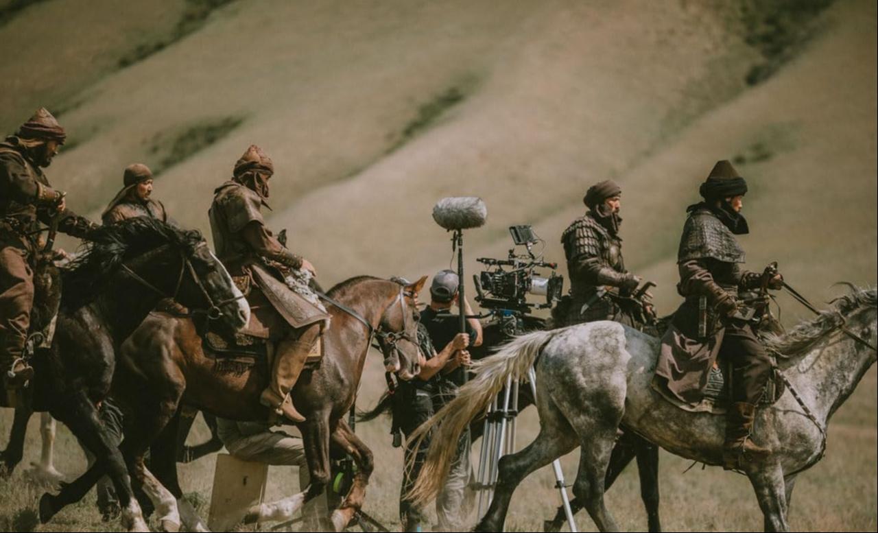 Behind the scenes of "Amir Temur: Rise of the Conqueror," as actors in period costume ride through a steppe landscape while a film crew captures the scene on location. (Photo by Mercy Hasselblad/McKess)