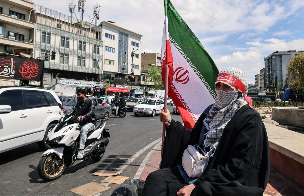 A woman sits with a national flag as people gather in Tehran's Revolution Square after the United States and Iran agreed to a two-week ceasefire, April 8, 2026. (AFP Photo)