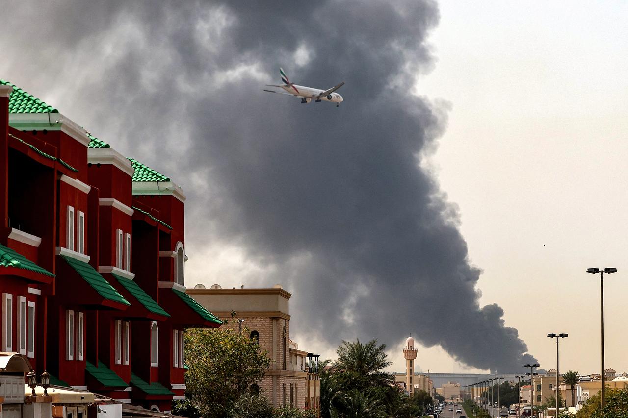 An Emirates aircraft prepares for landing as a smoke plume rises from an ongoing fire near Dubai International Airport in Dubai on March 16, 2026. (AFP Photo)