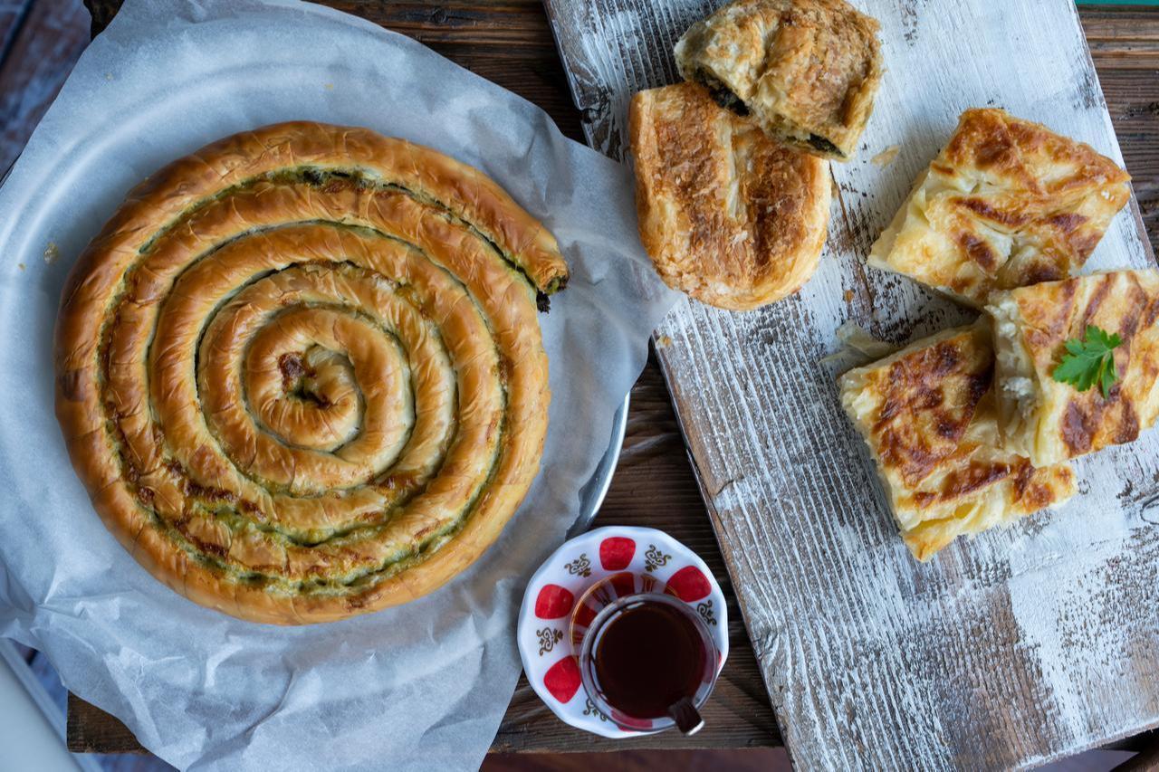 Different types of borek rest on a wooden table alongside traditional black tea, Istanbul, Türkiye, April 12, 2026. (Adobe Stock Photo)