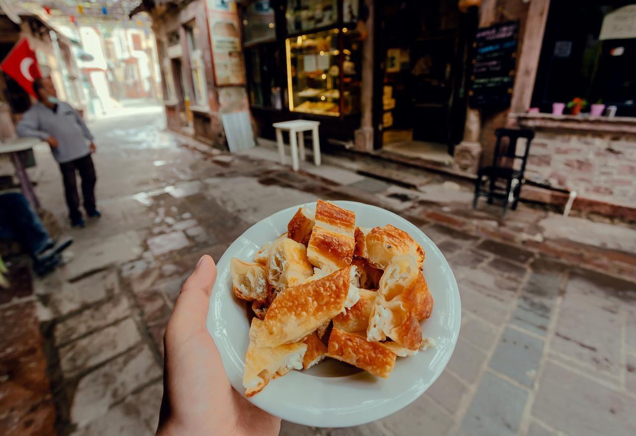 Freshly cut pieces of hot borek sit on a white plate held against a cobblestone street, Ayvalik, Türkiye, May 2, 2021. (Adobe Stock Photo)