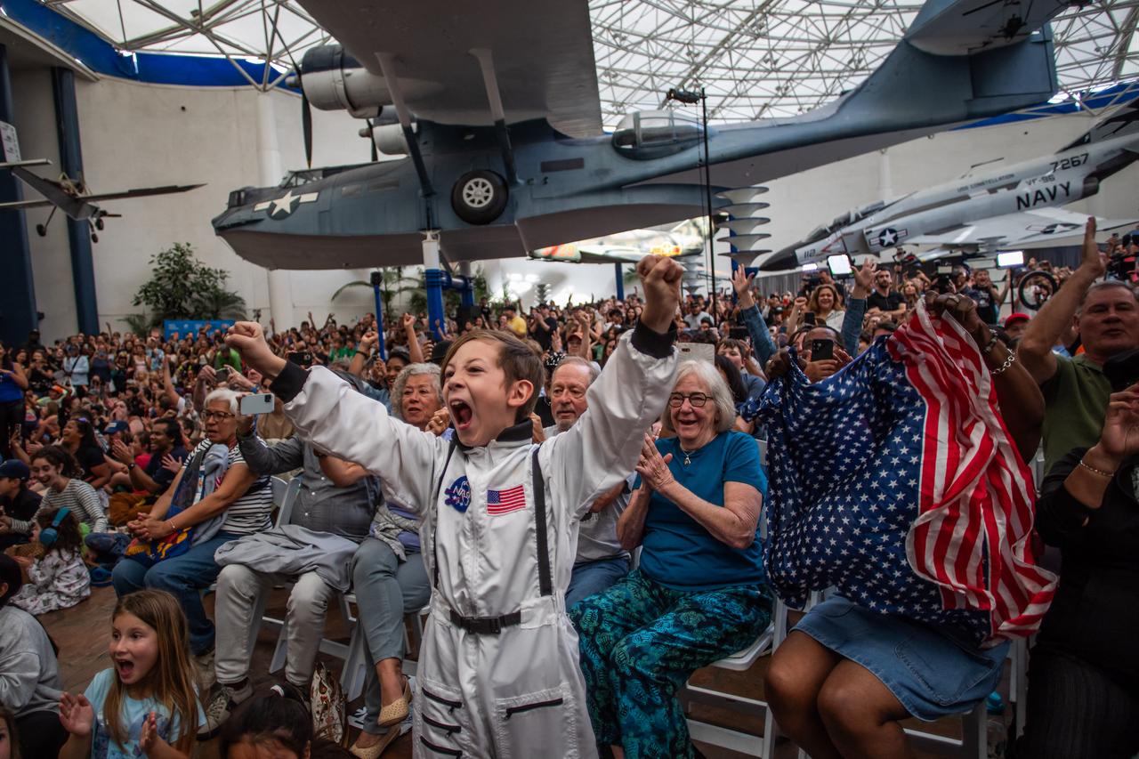 A young boy wearing an astronaut costume cheers next to a woman waving a flag as they watch a live broadcast of the return of the Artemis II crew members to Earth at the San Diego Air and Space Museum during a watch party for the crew's splash down in the Pacific Ocean, in San Diego, California, on April 10, 2026. (AFP Photo)