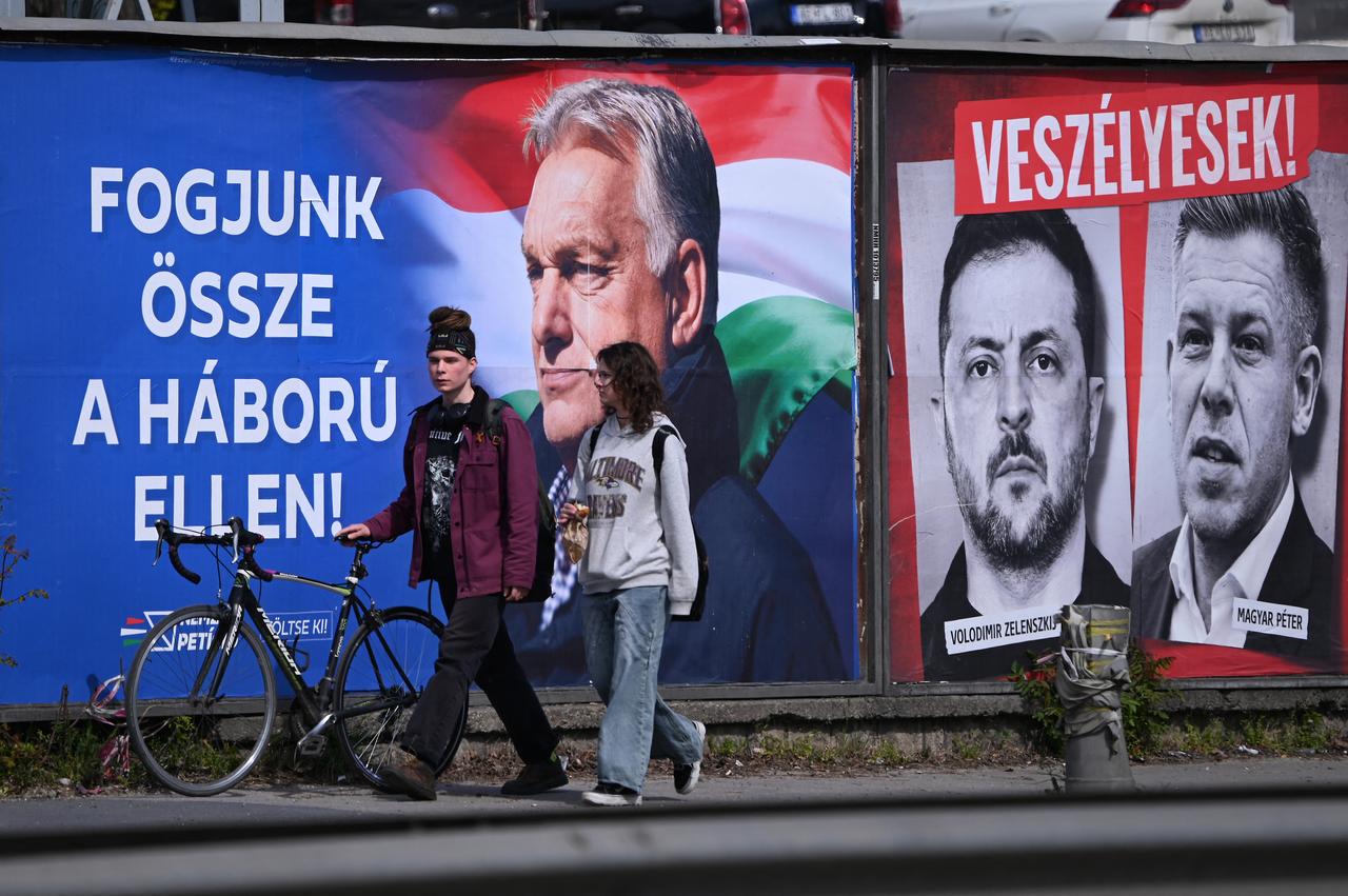 A young couple walk in front of billboards, featuring Hungarian Prime Minister Viktor Orban (L) with a text, reading 'Come together against the war' as portrait of Ukraine's President Volodymyr Zelensky and Hungarian opposition leader Peter Magyar with the text reading, 'They are dangerous',(top) and 'Let's stop them, just Fidesz (governor party)(R)' are seen in Budapest's 11th district on April 10, 2026. (AFP Photo)