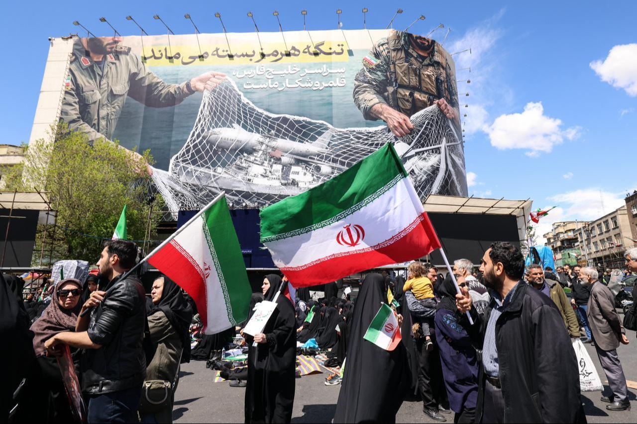 Iranians hold national flags beneath a large billboard reading "The Strait of Hormuz remains closed" as people gather in Tehran's Revolution Square, Iran, on April 8, 2026. (AFP Photo)