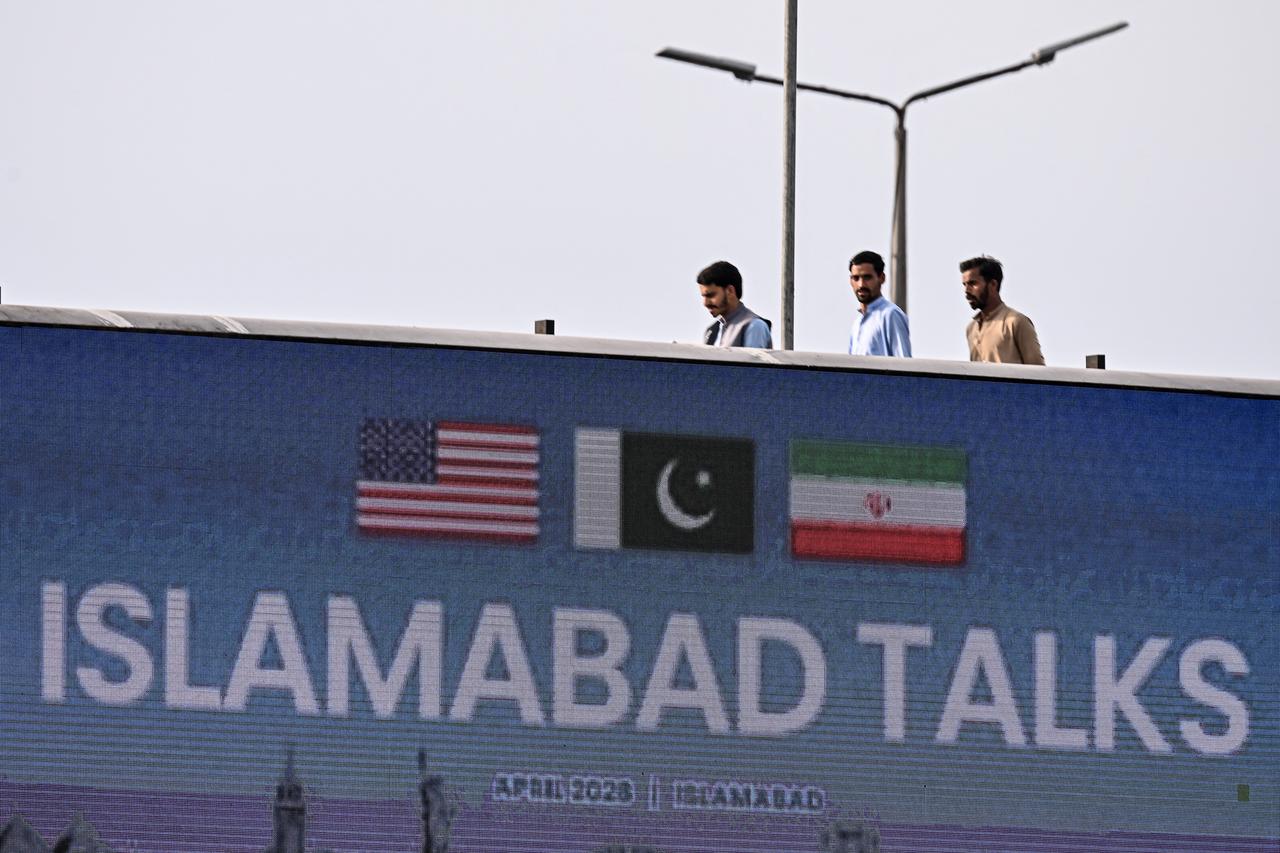 Youth walk behind a digital screen displaying news of US–Iran peace talks along a road in Islamabad, April 10, 2026. (AFP Photo)