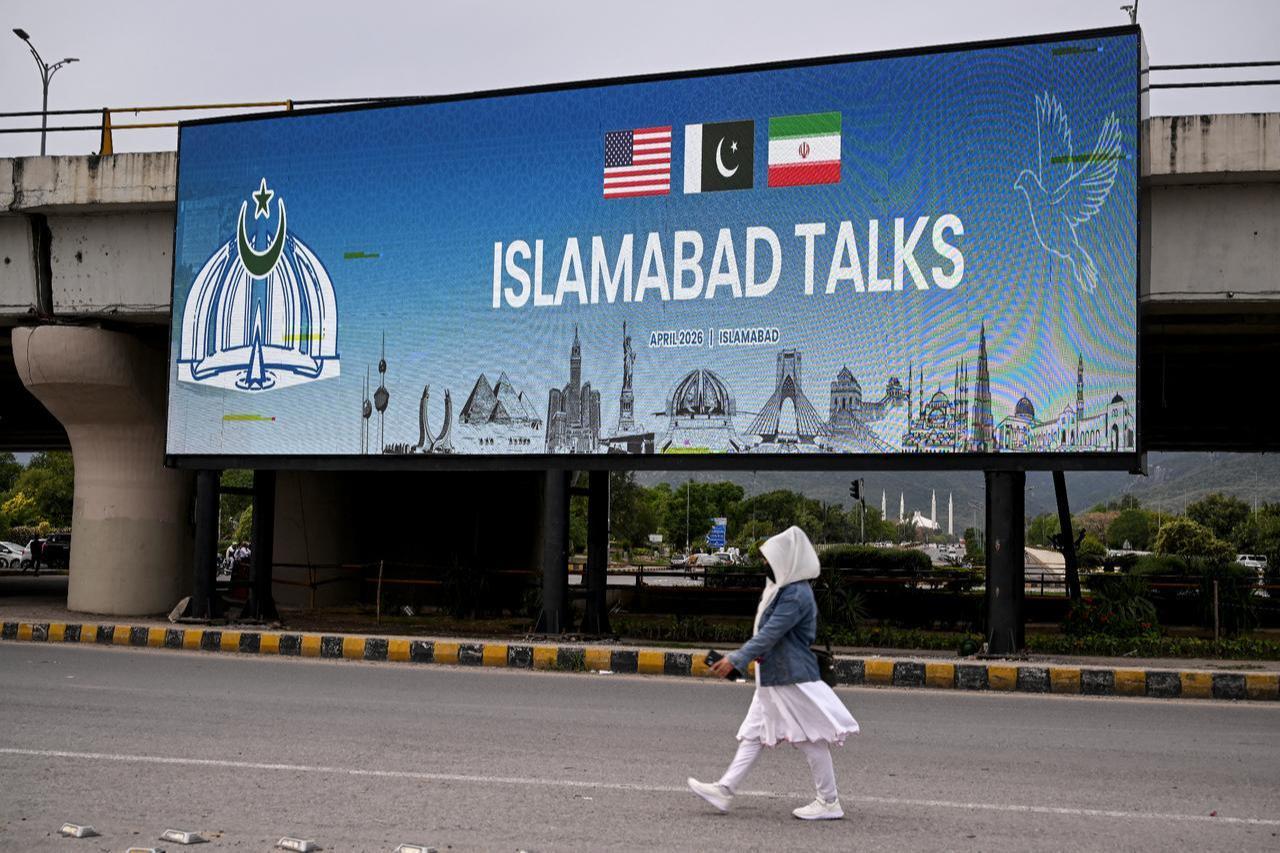 A woman walks past a digital screen displaying news of US–Iran peace talks along a road in Islamabad, April 10, 2026. (AFP Photo)