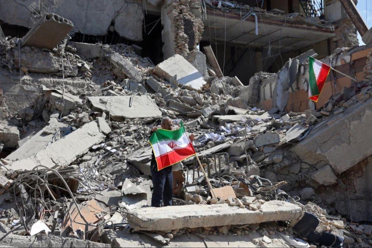 A man holds an Iranian flag amid the debris of a destroyed building following airstrikes in central Tehran, Iran, on March 4, 2026. (AFP Photo)