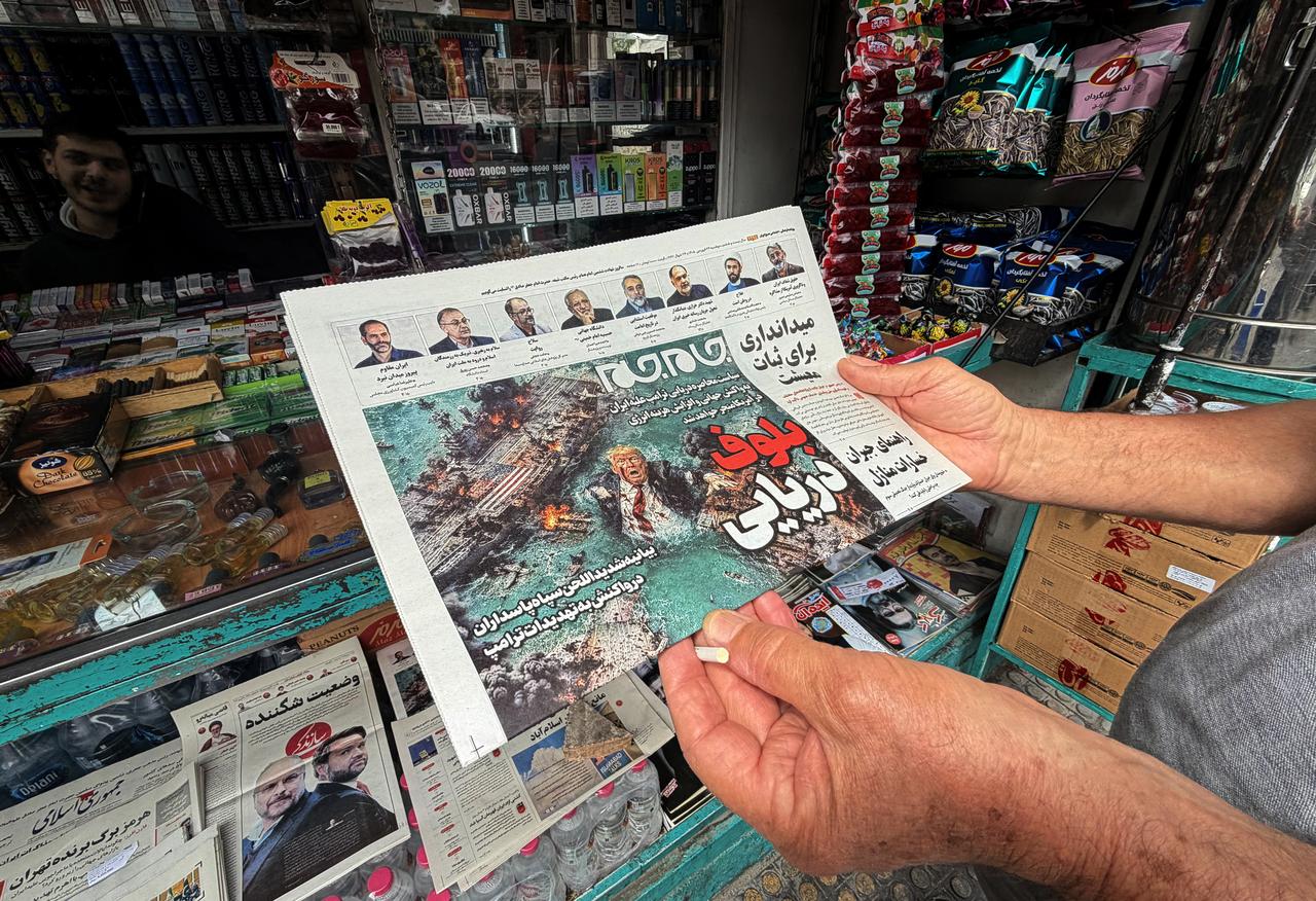 A man looks at the front page of the Jam Jam newspaper on sale at a newsstand, featuring a cartoon of US President Donald Trump drowning in the Strait of Hormuz, in Tehran, April 13, 2026. (AFP Photo)
