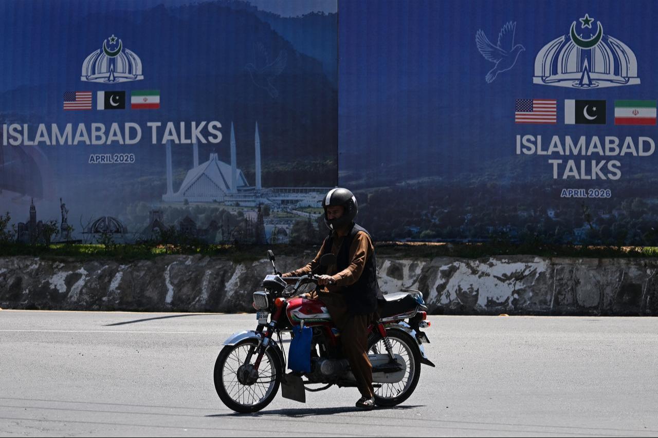 A commuter rides past a billboard for the US-Iran peace talks in Islamabad, April 13, 2026. (AFP Photo)