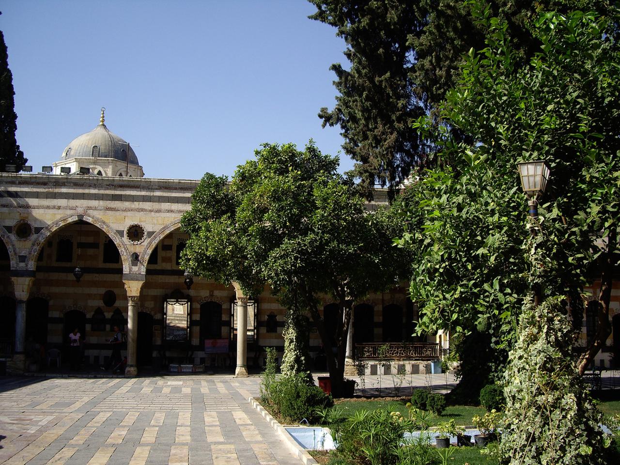 Al-Azm Palace courtyard with stone arches and greenery in Damascus, Syria. (Photo via Wikimedia)