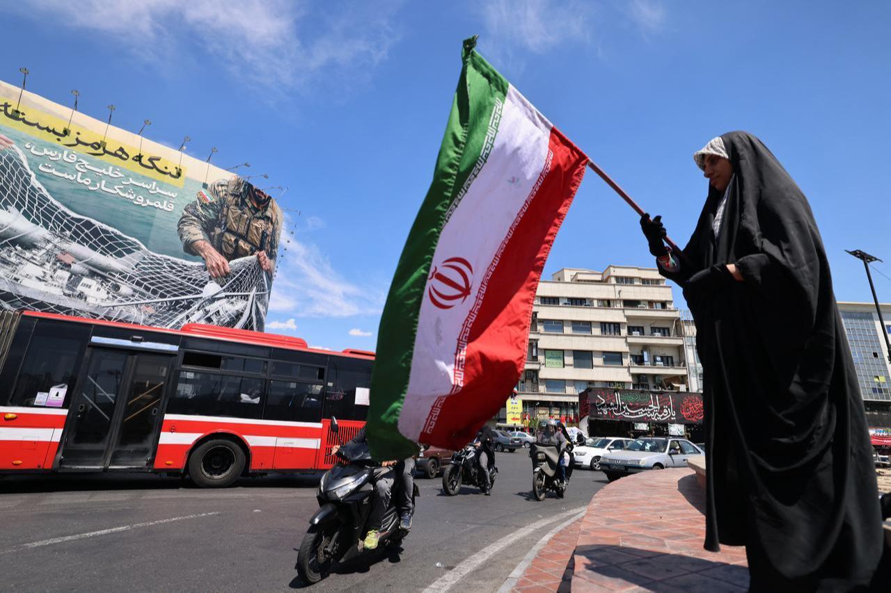 A woman waves Iran's national flag in front of a giant billboard reading 'The Strait of Hormuz remains closed' at the Revolution Square in Tehran, April 12, 2026. (AFP Photo)