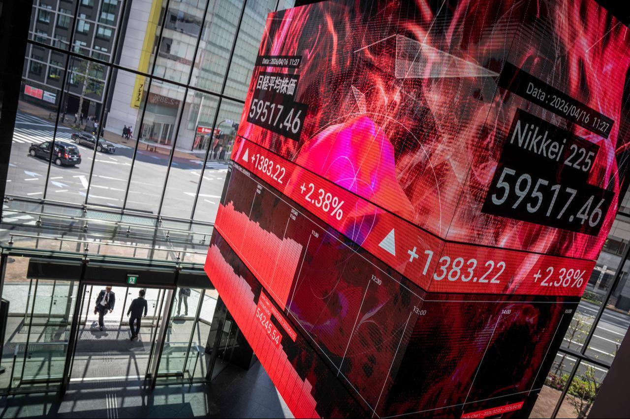 People walk in and out of a building as an electronic quotation board displays the Nikkei Stock Average on the Tokyo Stock Exchange in Tokyo, April 16, 2026. (AFP Photo)