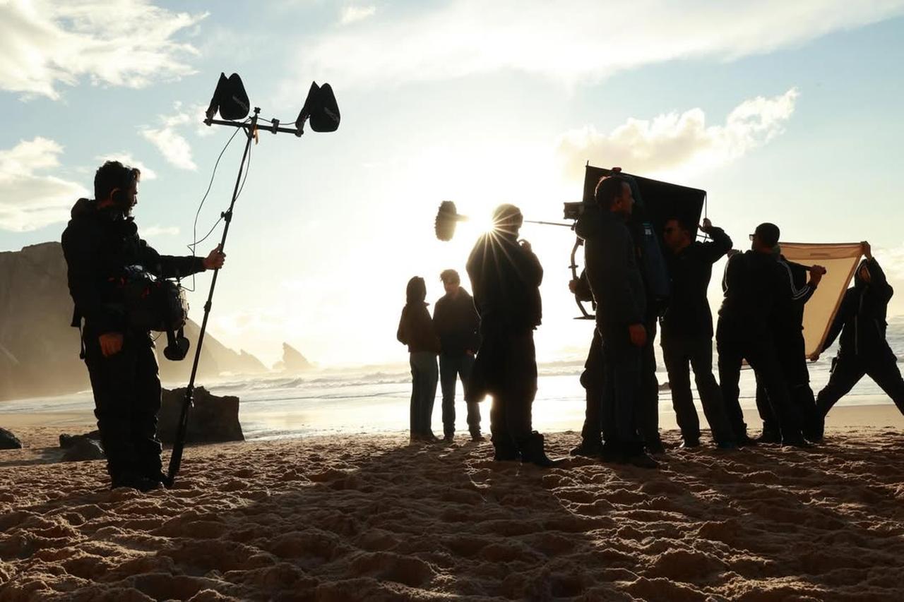 Film crew members prepare lighting and sound equipment on a beach set, offering a behind-the-scenes look at the production process. (Photo via Instagram/@cansudere)