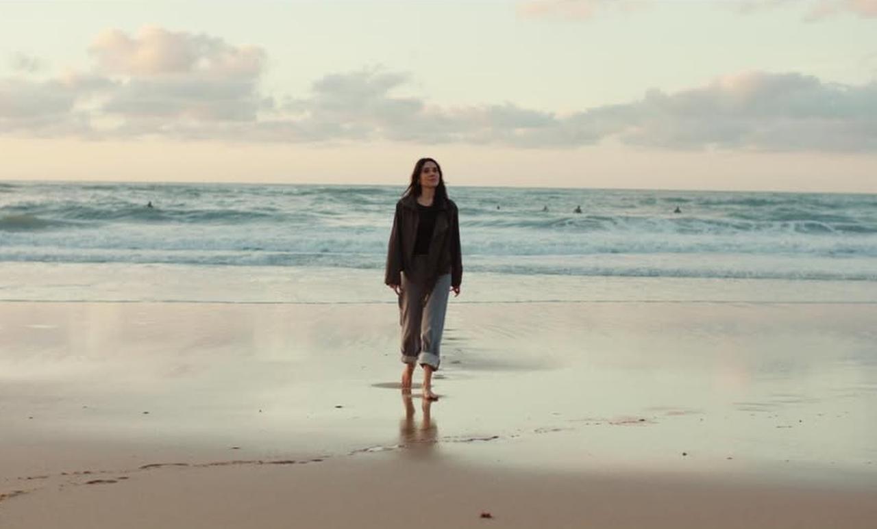 Cansu Dere walks barefoot along the shoreline as waves roll in, reflecting the film’s emotional tone and seaside backdrop. (Photo via Instagram/@cansudere)
