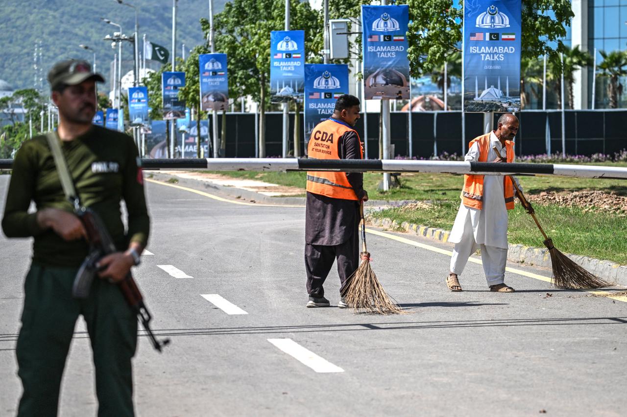 Sanitation workers sweep a road as a security personnel stands guard near the Serena Hotel in Islamabad on April 19, 2026. (AFP Photo)