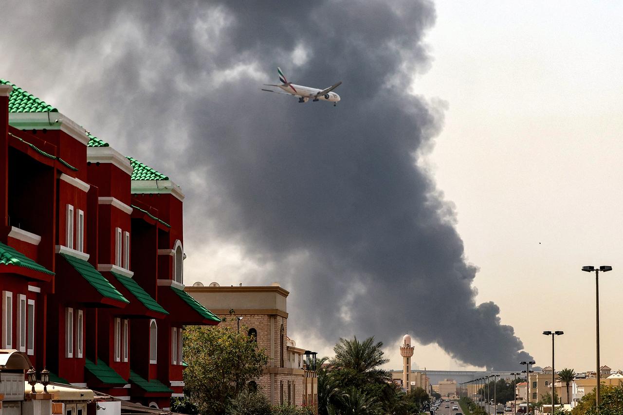 An Emirates aircraft prepares for landing as a smoke plume rises from an ongoing fire near Dubai International Airport in Dubai on March 16, 2026. (AFP Photo)